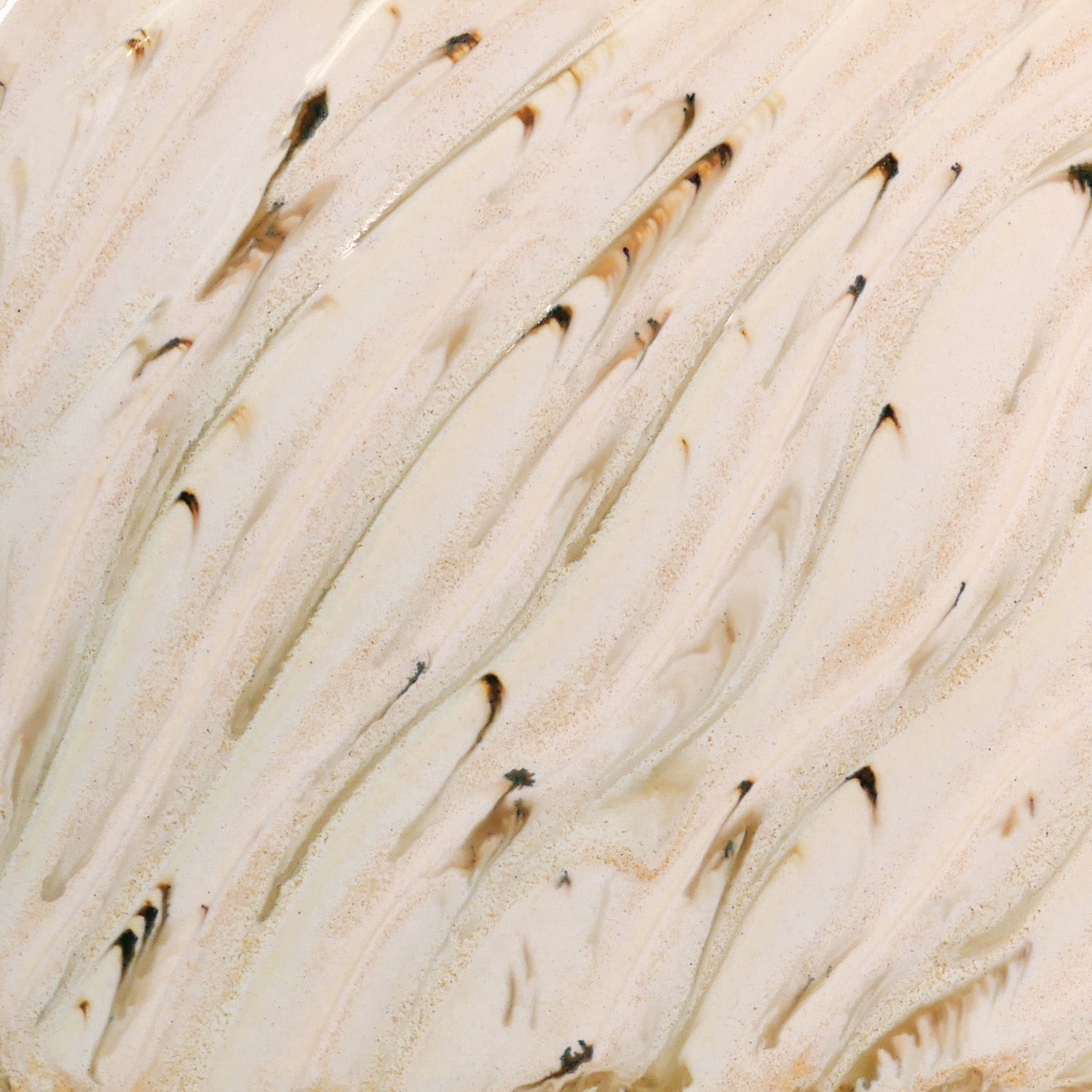 Glossy cream glaze with runny dark specks, breaking on texture with peachy float, great for layering. Amaranth Stoneware Canada.
