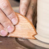 A wood potter's rib with a curved arc, straight edge, and unique V- and U-shaped notches for shaping clay. Amaranth Stoneware Canada.